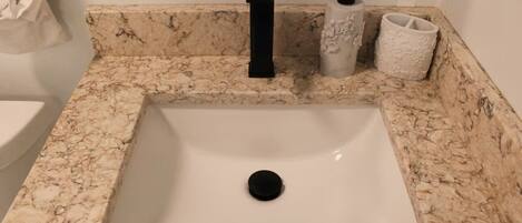 Un baño con un lavamanos de mármol, un grifo negro y dos jarrones decorativos.