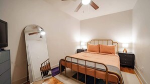Ein Schlafzimmer mit einem Metallbett, einem Deckenventilator, einem großen Spiegel und Nachttischlampen.