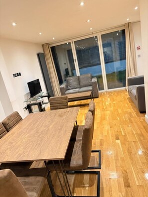 Een moderne woonkamer met een houten eettafel, banken en een grote schuifpui die leidt naar een balkon.