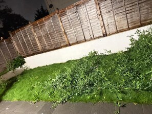 A garden area with a wooden fence, a grassy patch, and a paved walkway.