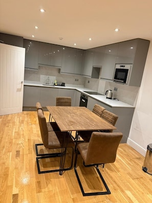 A modern kitchen with grey cabinets, a wooden dining table, and a built-in oven.
