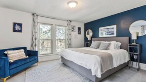 Una camera da letto con un letto, un divano blu, un'ampia finestra e una parete decorata con opere d'arte.