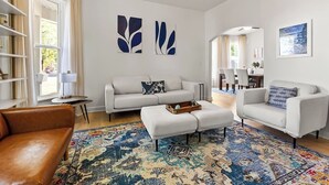 Un ampio soggiorno con un grande tappeto, un divano, un tavolino da caffè e una poltrona in pelle marrone. Sono presenti opere d'arte astratte alle pareti e un quadro incorniciato.