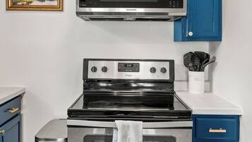 A kitchen with a stainless steel microwave, a Whirlpool stove, and an oven. There are blue cabinets and a white countertop.