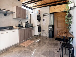A modern kitchen with a stove, sink, and washing machine, wooden ceiling, and a small dining area with stools.