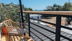 A balcony with wicker furniture, a potted plant, and a view of the sea and buildings. - Bright Room with Private Bathroom & Balcony Ocean View (San Felipe)