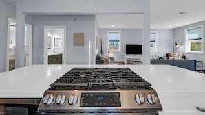 A modern kitchen with a stainless steel stove, a large white countertop, and a view into a living area with a TV and seating. - Modern Duplex, Sleeps 10, Dog Friendly + Fenced Yard, Full Kitchen & Kitchenette (Galveston)