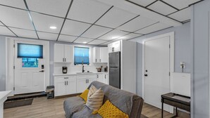 A modern kitchen with white cabinets, a stainless steel refrigerator, and a window with blinds. - Modern Duplex, Sleeps 10, Dog Friendly + Fenced Yard, Full Kitchen & Kitchenette (Galveston)