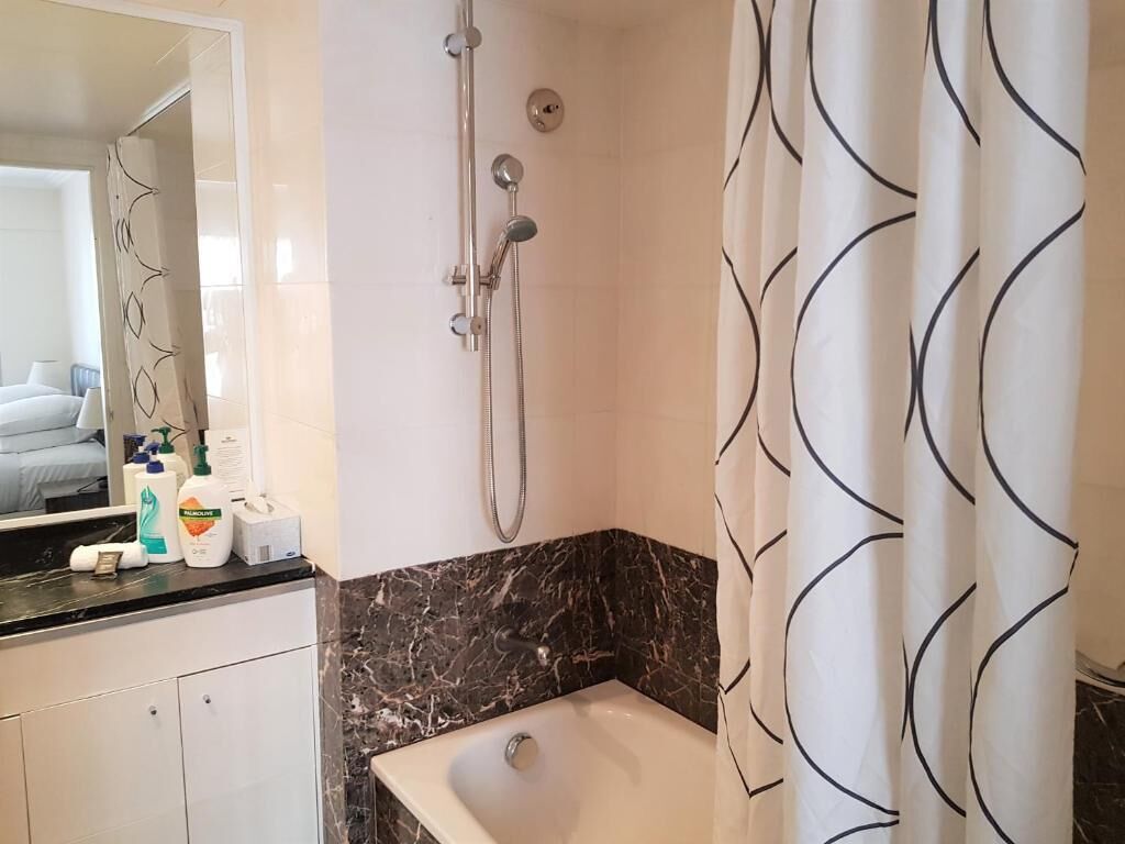 A bathroom with a shower, a bathtub, and a mirror. There are toiletries on the counter.