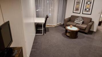 A living room with a sofa, a coffee table, a TV, and a dining area with a chair and table.