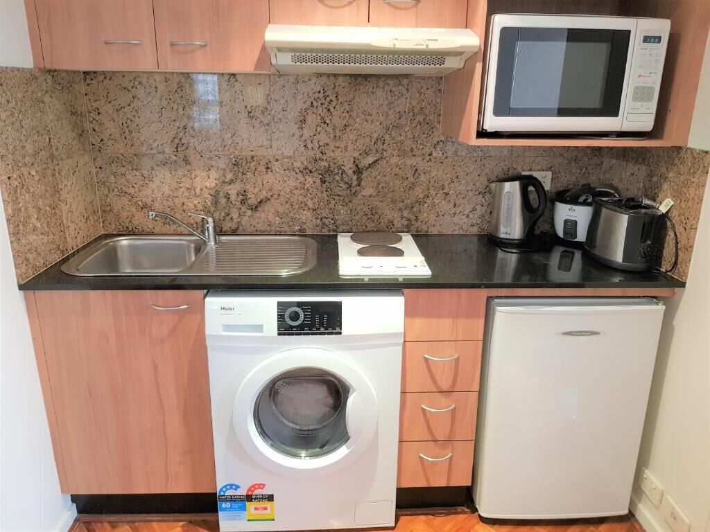Een kleine keuken met een magnetron, spoelbak, fornuis en een wasmachine.