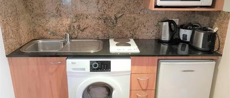 Een kleine keuken met een magnetron, spoelbak, fornuis en een wasmachine.
