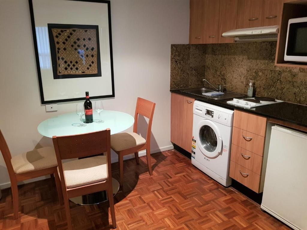 A compact kitchen with a washing machine, a microwave, and a dining area with two chairs and a table.