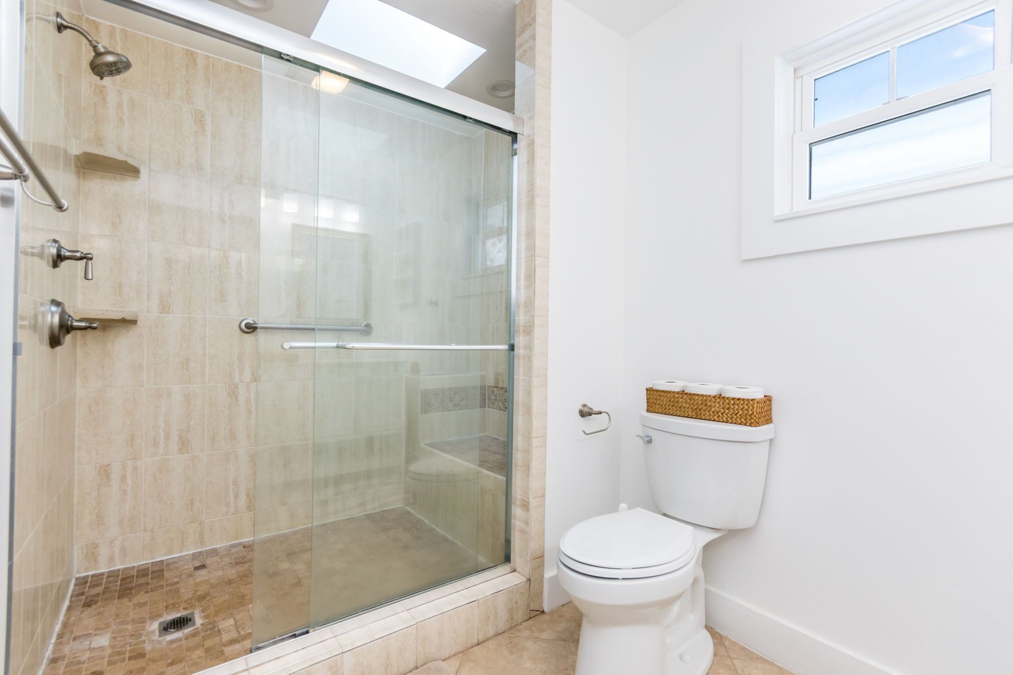 A bathroom with a glass-enclosed shower, a white toilet, and a window.