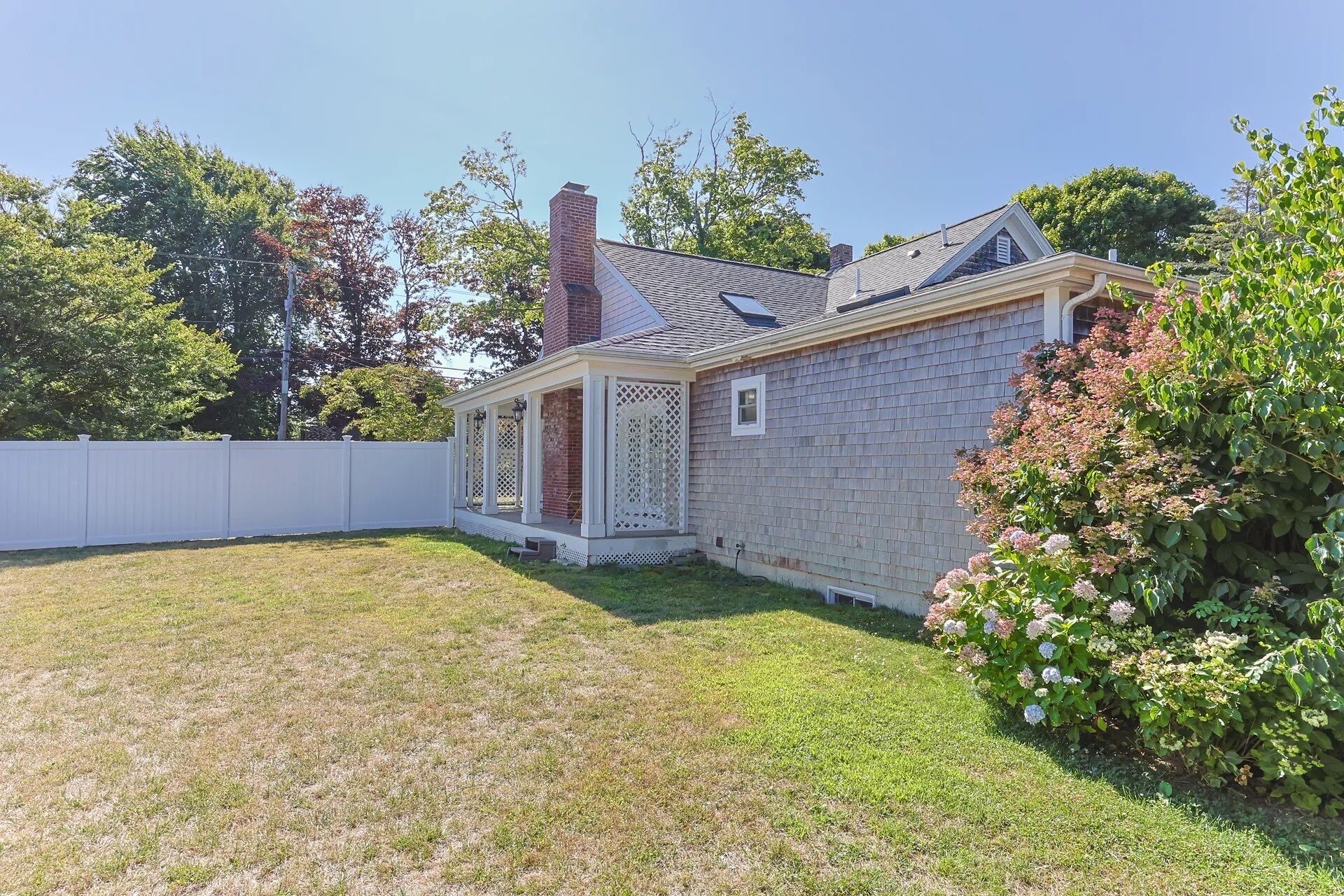 A single-story house with a covered porch, a brick chimney, and a fenced backyard.