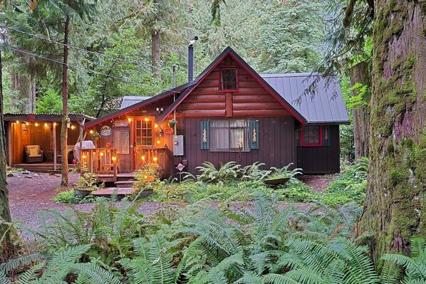 A cabin with a porch, a small attached structure, and a forested backdrop.