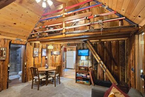A wooden interior with a dining area, a television, and skis stored on a rack.