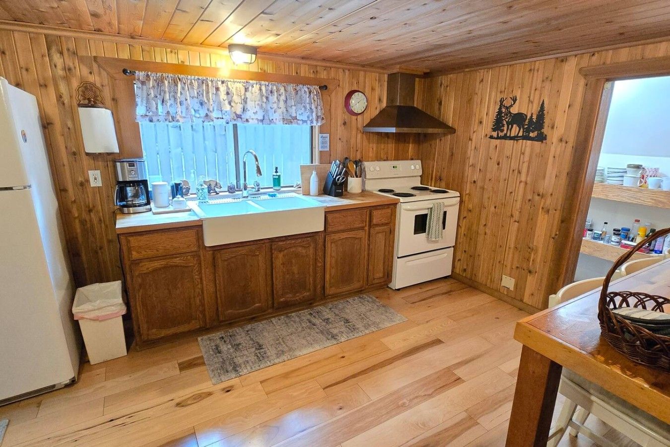A kitchen with wooden cabinets, a stove, a sink, and a window with a floral curtain.