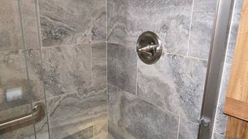 A shower with a rain showerhead, a handheld showerhead, and a glass door.