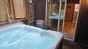Ein Whirlpool mit einer Holzdiele und einer Glastür zu einem Badezimmer mit Waschbecken und Ablage für Toilettenartikeln.
