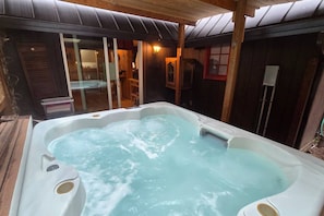 A hot tub in a wooden cabin with a glass door leading to a room.