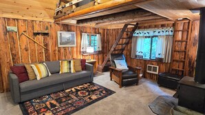 Ein gemütliches Blockhaus-Interieur mit Holzausstattung, einer Couch, einem Sessel, einem Teppich und einer Leiter.