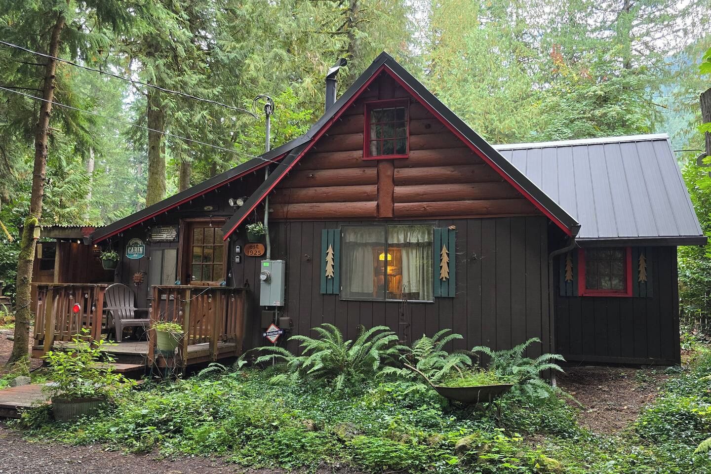 A cabin with a porch, a small attached structure, and a wheelbarrow filled with plants.