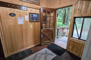 A wooden interior with a door leading to an outdoor deck, a welcome mat, and a 'Kindly REMOVE YOUR SHOES' sign.