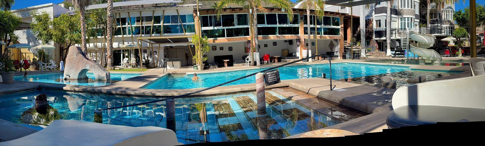 A hotel pool area with multiple swimming pools, lounge chairs, and a slide.