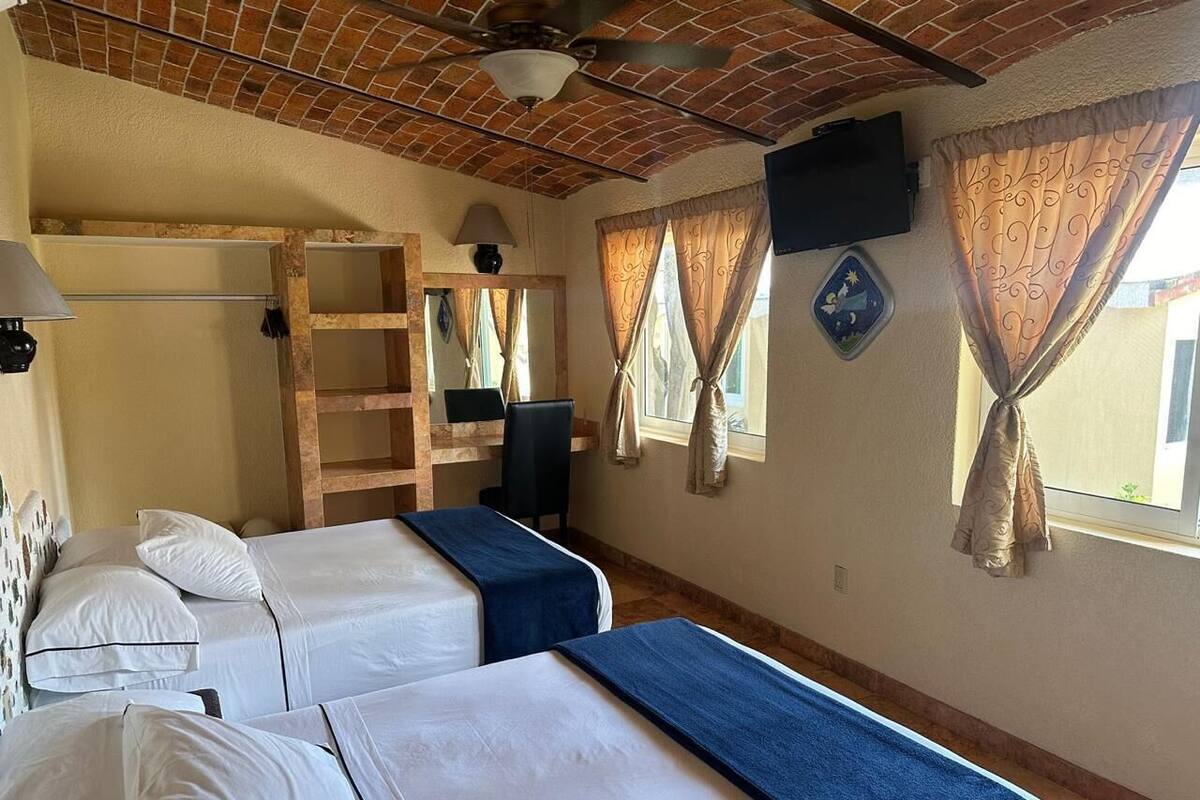 A room with two beds, a wooden ladder, a television, and curtains.
