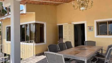 Un patio cubierto con una mesa y sillas, una araña y una puerta que da a un espacio interior.