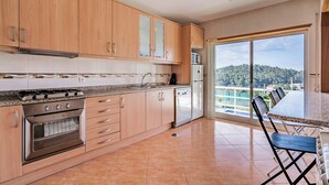 A modern kitchen with wooden cabinets, a gas stove, a dishwasher, and a large window overlooking a scenic view. - Casal do Porto - A vacation retreat (Lourido)