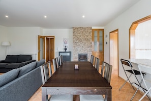 Un salon moderne avec une grande table à manger en bois foncé, des canapés gris et un mur d’accent en pierre.