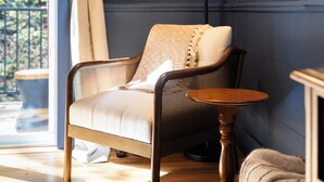 A room with a wooden floor, a chair with a cushion, a table, and a lamp.
