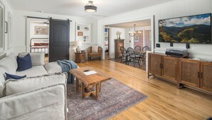 A spacious living room with a wooden floor, a large TV, and a dining area with chairs and a table.