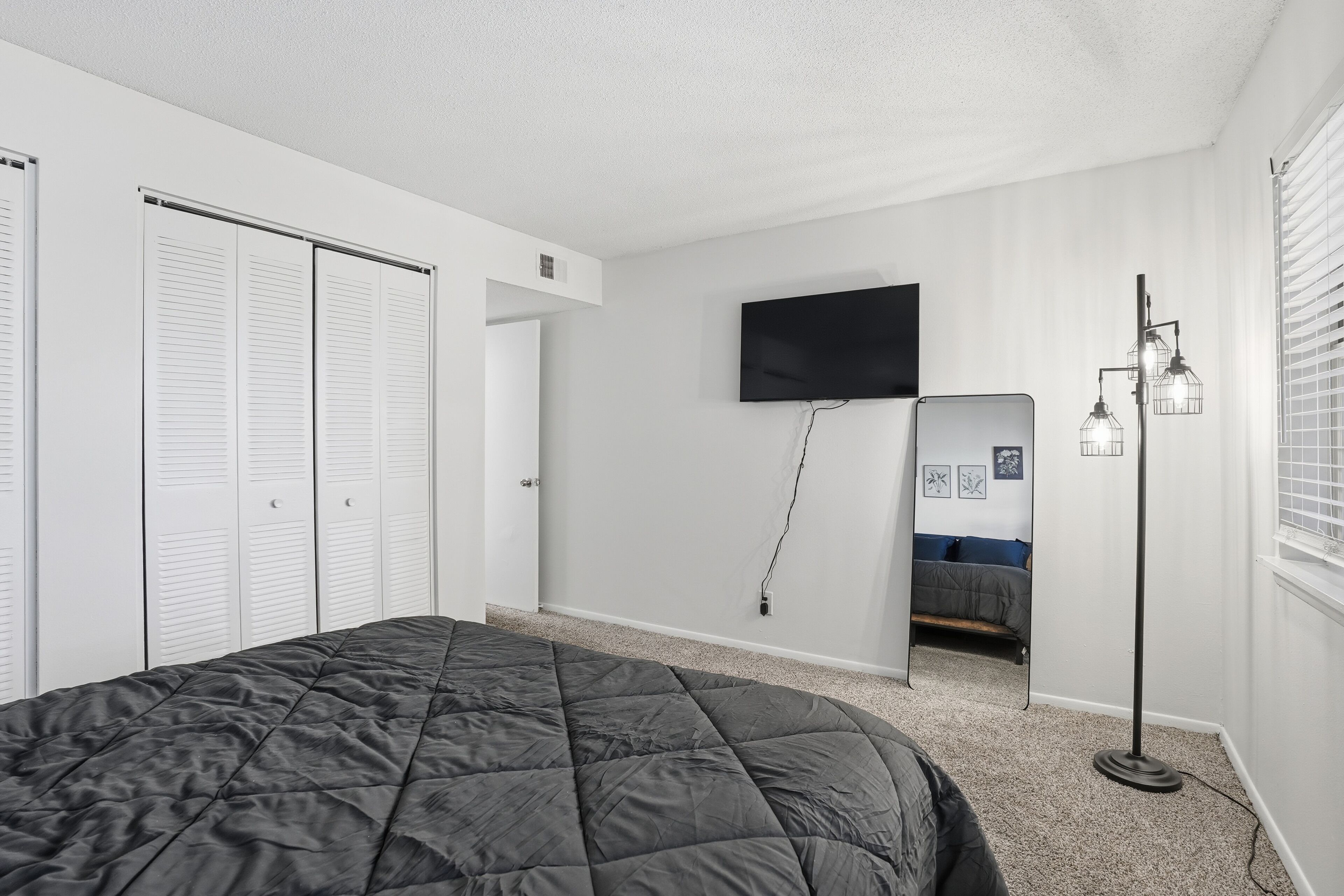 A bedroom with a bed, a TV, a mirror, and a floor lamp.