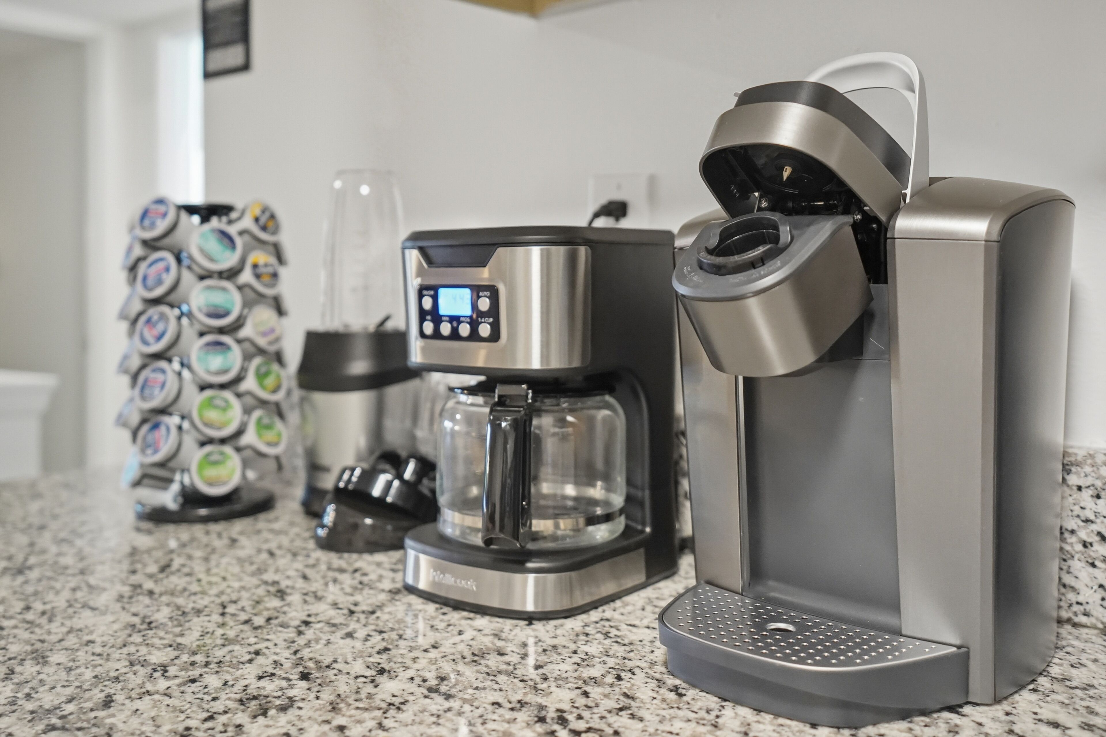 A coffee maker with a digital display, a glass carafe, and a drip tray on a granite countertop.