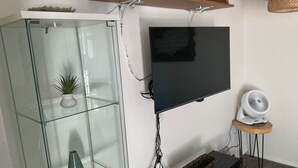 A living room with a glass cabinet, a flat-screen TV, a small fan, and a wooden shelf with decorative items. - Contemporary, marine 2bd/1ba Apartment in Kent (kent)
