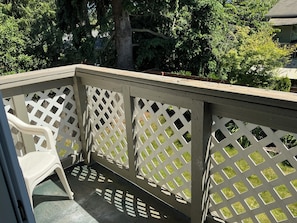 A wooden deck with a lattice railing, a plastic chair, and a tree in the background.