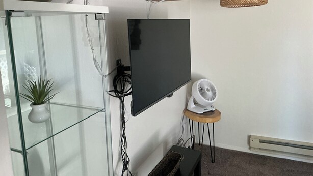 A living room with a TV mounted on the wall, a glass cabinet, a small table with a fan, and a wicker lamp. - Contemporary, marine 2bd/1ba Apartment in Kent (kent)