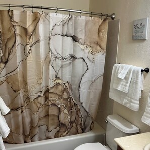 A bathroom with a marble-patterned shower curtain, a toilet, and a towel rack with towels. - Contemporary, marine 2bd/1ba Apartment in Kent (kent)