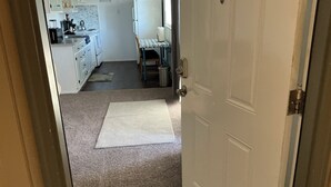 A hallway leading to a kitchen with white cabinets, a refrigerator, and a dining table with chairs. - Contemporary, marine 2bd/1ba Apartment in Kent (kent)