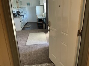 A hallway leading to a kitchen with white cabinets, a refrigerator, and a dining table with chairs.