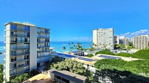 Un hotel a più piani con balconi affacciati su una spiaggia e l'oceano, pannelli solari sul tetto e un cielo azzurro intenso.