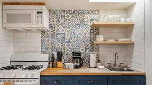 A kitchen with a gas stove, microwave, and a patterned backsplash. There are cabinets, a sink, and a coffee maker on the counter.
