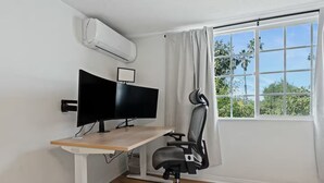 A corner office with a desk, two monitors, a chair, and a window with curtains.