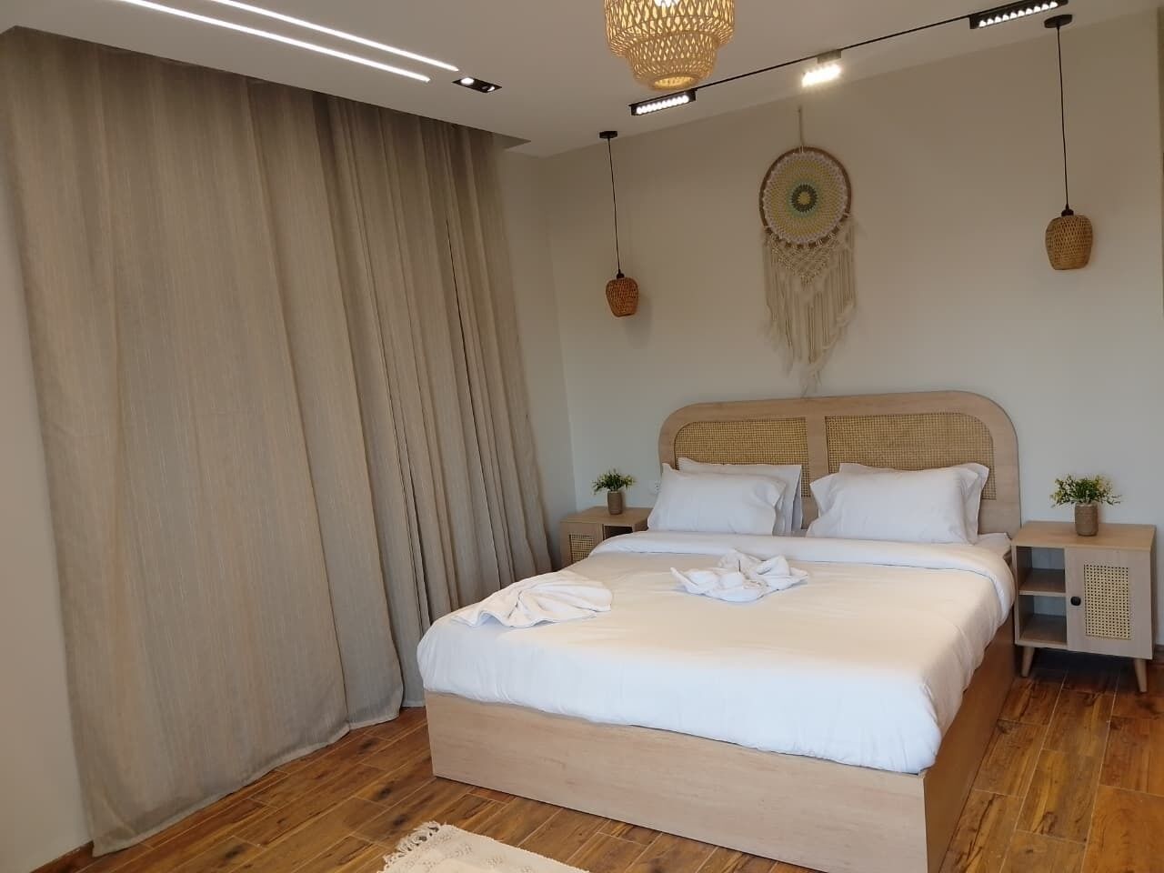 A neatly made bed with white linens, a wooden headboard, and a bedside table with a plant.