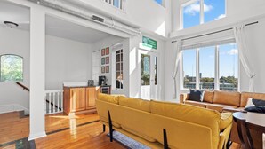 A spacious living area with a yellow sofa, wooden flooring, a staircase, and a view of the city.