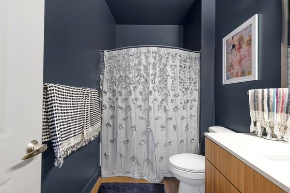A bathroom with a shower curtain, a toilet, a sink, and a towel rack.