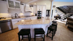 A modern kitchen with a large island, white cabinetry, and a staircase leading to an upper level. - THE BEST VIEW! On the Golf Course with Pool! (Lake Havasu City)